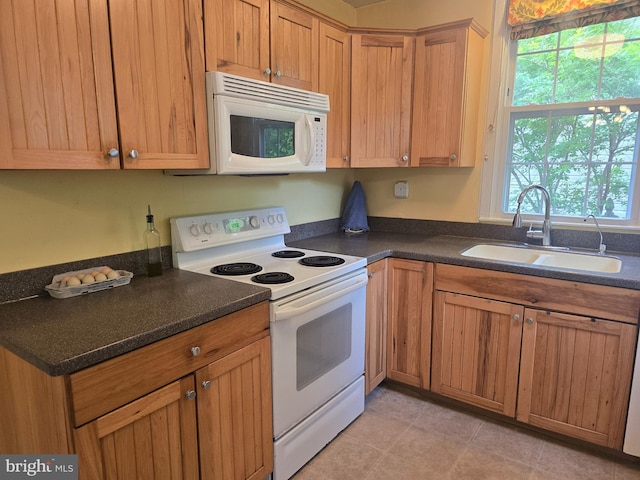 kitchen with white appliances, a sink, dark countertops, and brown cabinetry