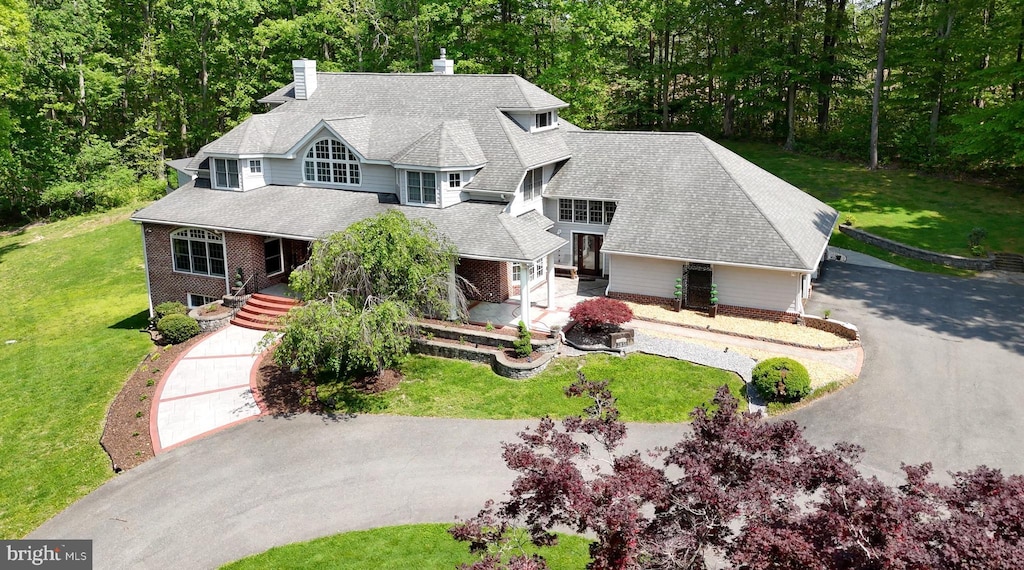 view of front facade with a view of trees, driveway, a chimney, and a front yard
