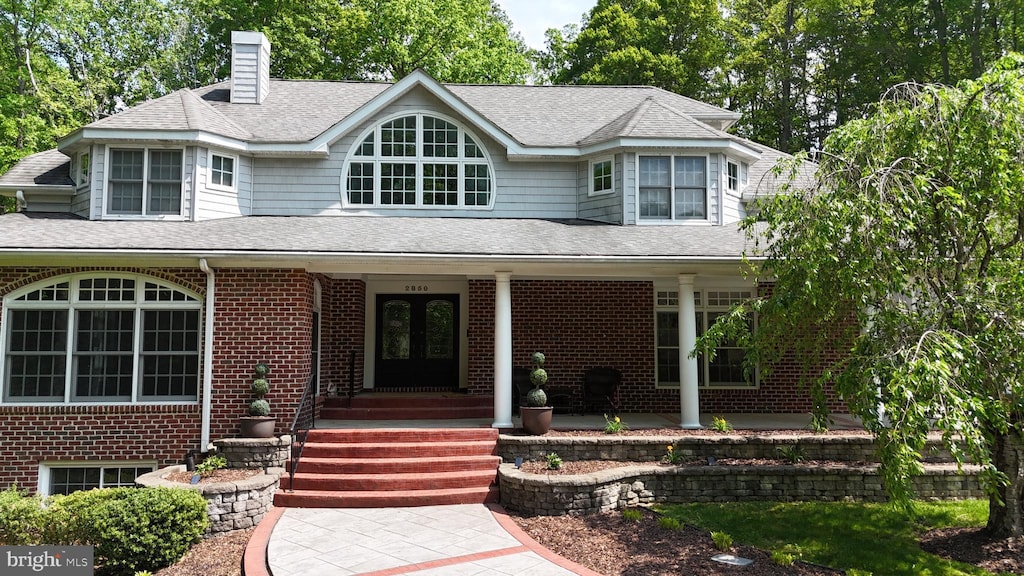 view of front of home with french doors, brick siding, roof with shingles, and a chimney