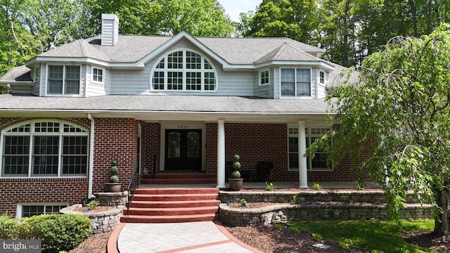 view of front of home with french doors, brick siding, roof with shingles, and a chimney