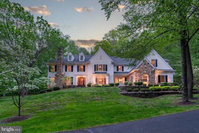 view of front facade featuring stone siding, french doors, stucco siding, a chimney, and a lawn
