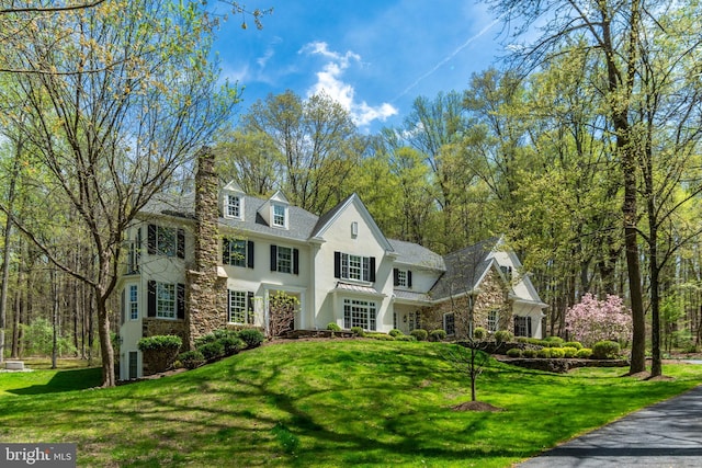 view of front facade featuring stone siding, stucco siding, a chimney, and a front yard