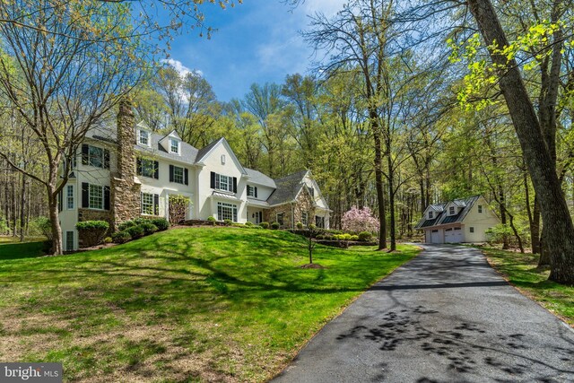 view of front of home featuring stone siding, a garage, stucco siding, a front yard, and an outbuilding