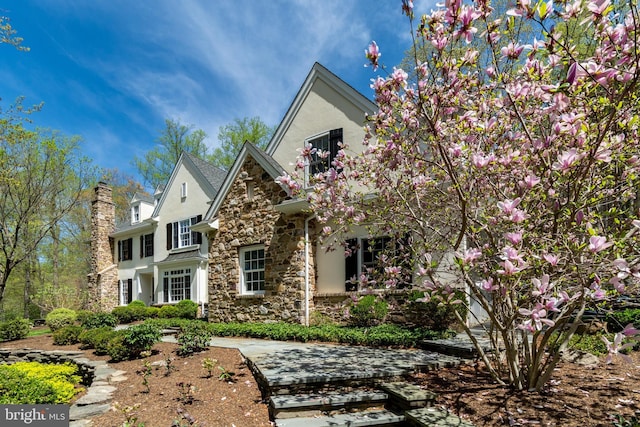 craftsman-style house featuring stucco siding, a chimney, and stone siding