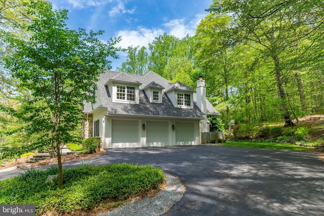 view of front facade featuring an attached garage, driveway, stucco siding, a chimney, and a shingled roof