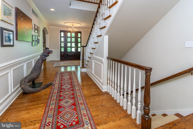 doorway to outside featuring a notable chandelier, crown molding, visible vents, a decorative wall, and arched walkways