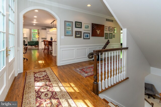 entrance foyer featuring arched walkways, crown molding, visible vents, and wood finished floors