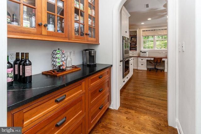 bar with stainless steel double oven, visible vents, dark wood finished floors, crown molding, and arched walkways