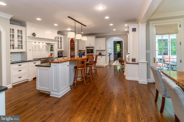 kitchen featuring arched walkways, ornamental molding, stainless steel oven, and white cabinets