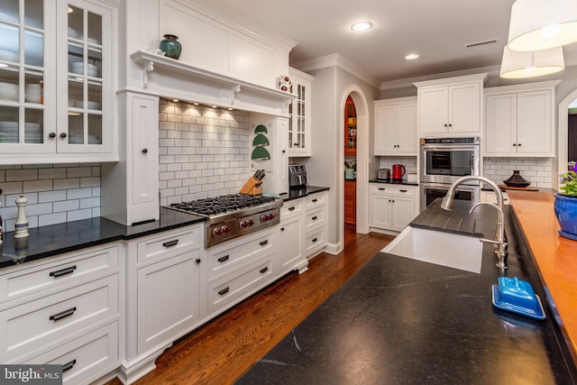 kitchen featuring ornamental molding, a sink, decorative backsplash, arched walkways, and stainless steel appliances