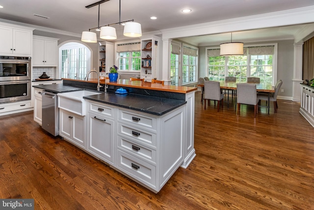 kitchen with a sink, stainless steel appliances, a wealth of natural light, white cabinetry, and ornamental molding