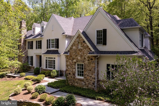 view of front of property featuring stone siding, stucco siding, roof with shingles, and a chimney