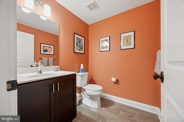 bathroom featuring visible vents, wood finished floors, vanity, baseboards, and toilet
