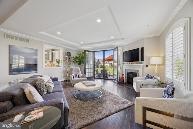 living area featuring visible vents, a glass covered fireplace, wood finished floors, and a tray ceiling