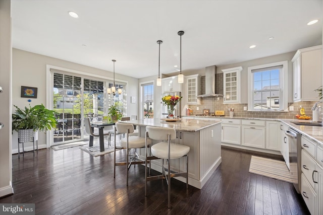 kitchen featuring decorative backsplash, a kitchen island, appliances with stainless steel finishes, white cabinets, and wall chimney exhaust hood