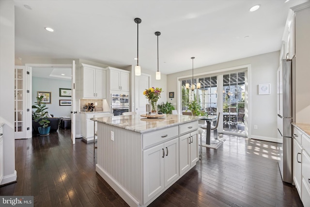 kitchen with appliances with stainless steel finishes, dark wood finished floors, white cabinetry, baseboards, and pendant lighting