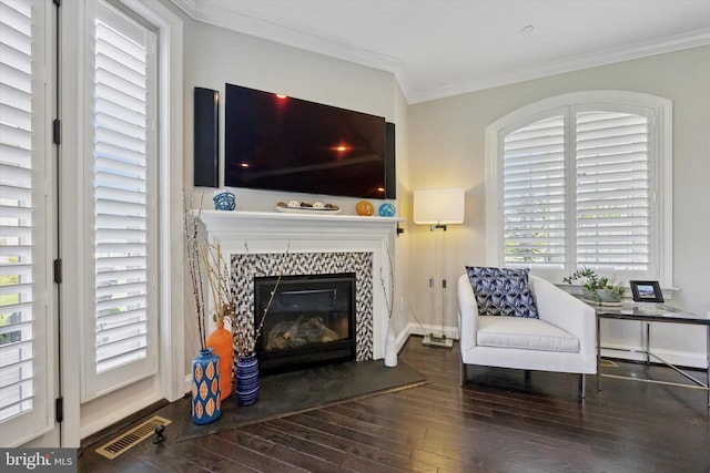 living area featuring visible vents, ornamental molding, wood finished floors, baseboards, and a tiled fireplace