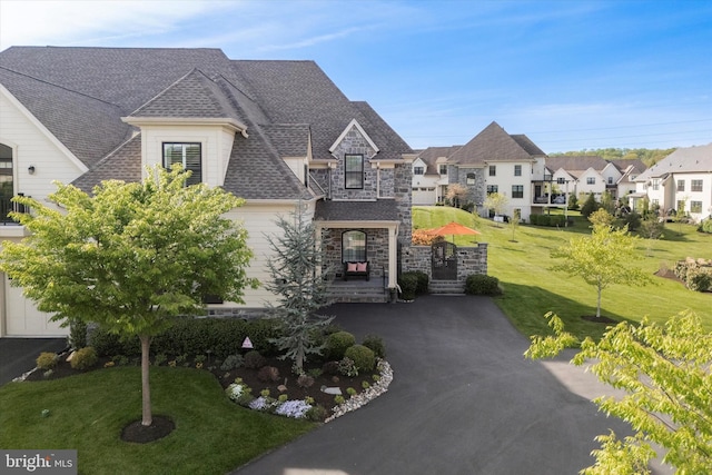 french country style house featuring roof with shingles, a residential view, stone siding, and a front lawn