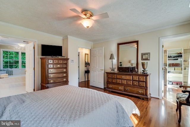 bedroom featuring connected bathroom, a walk in closet, a textured ceiling, hardwood / wood-style floors, and ornamental molding