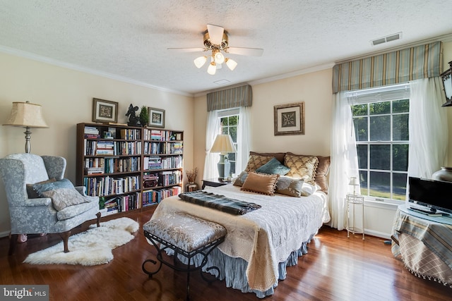 bedroom with visible vents, a textured ceiling, crown molding, and wood finished floors