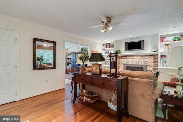 living room featuring ornamental molding, wood finished floors, a fireplace, baseboards, and ceiling fan