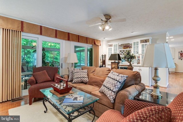 living room with light wood-style floors, ornamental molding, a ceiling fan, and a textured ceiling
