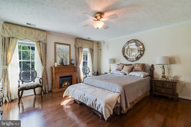 bedroom with visible vents, a textured ceiling, dark wood-type flooring, and a glass covered fireplace