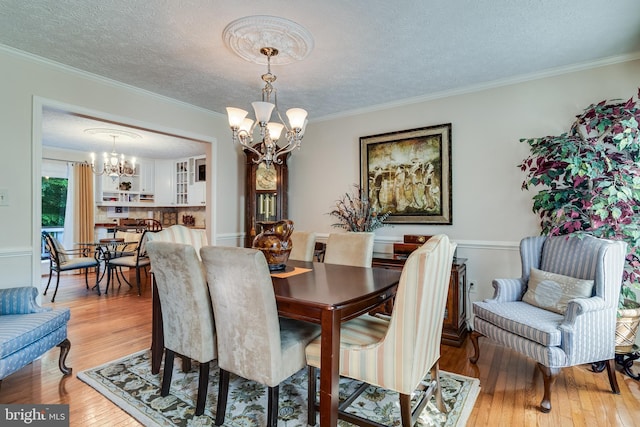 dining area featuring light wood-style floors, ornamental molding, a textured ceiling, and a chandelier