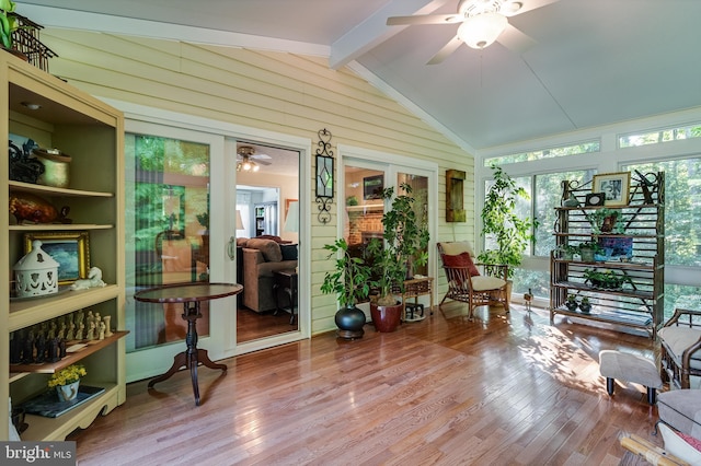 sunroom with plenty of natural light, wood walls, wood finished floors, and vaulted ceiling with beams