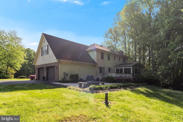 exterior space featuring a front lawn, brick siding, a garage, aphalt driveway, and a sunroom