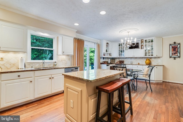 kitchen with a center island, light stone countertops, a sink, light wood finished floors, and a notable chandelier