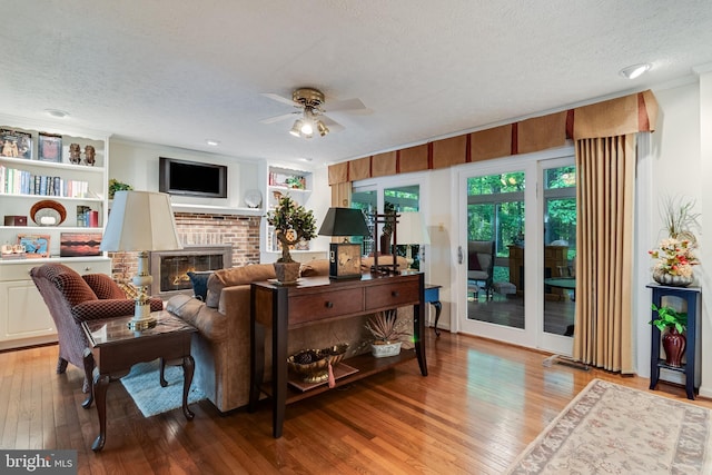 living room with a brick fireplace, a textured ceiling, ceiling fan, and light wood finished floors
