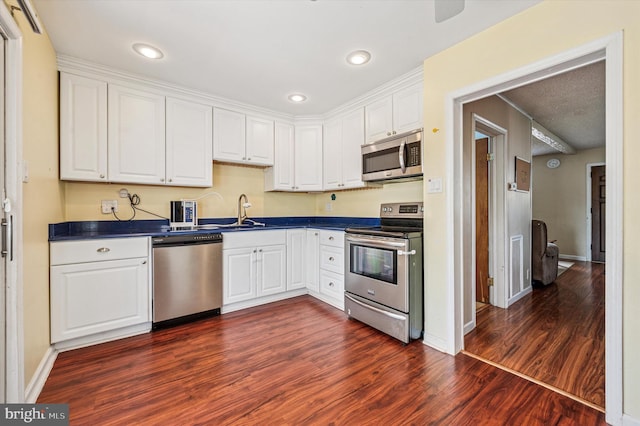 kitchen with dark countertops, appliances with stainless steel finishes, dark wood-style floors, and white cabinetry
