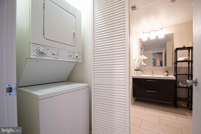 washroom with laundry area, a sink, stacked washing maching and dryer, and visible vents