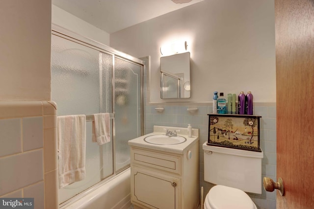 bathroom featuring vanity, wainscoting, shower / bath combination with glass door, toilet, and tile walls