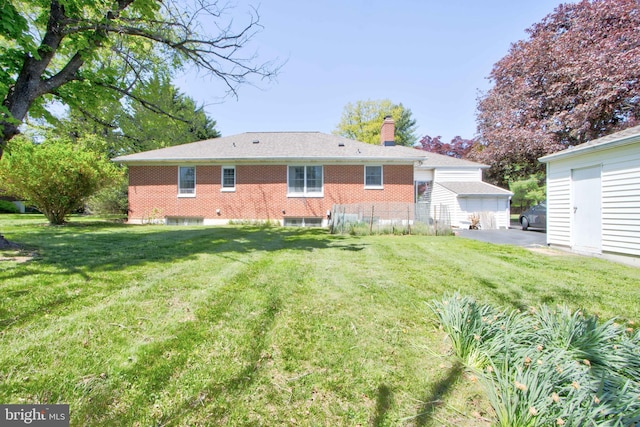 back of property with an outdoor structure, fence, a chimney, brick siding, and a lawn
