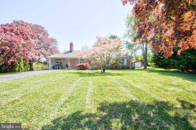 single story home featuring aphalt driveway, a shed, a front yard, an outbuilding, and a carport