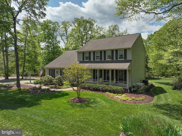 colonial-style house featuring covered porch, a front yard, and cooling unit