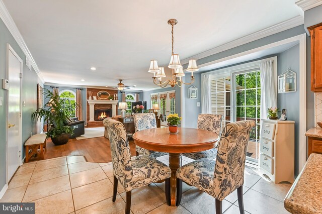 dining space with crown molding, ceiling fan with notable chandelier, a warm lit fireplace, and light tile patterned flooring