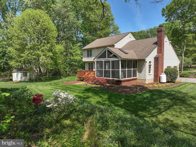 back of property with roof with shingles, a yard, a chimney, a sunroom, and an outbuilding