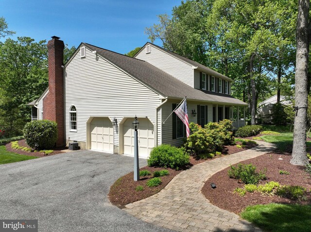 view of side of property featuring a shingled roof, central AC, a garage, a chimney, and driveway
