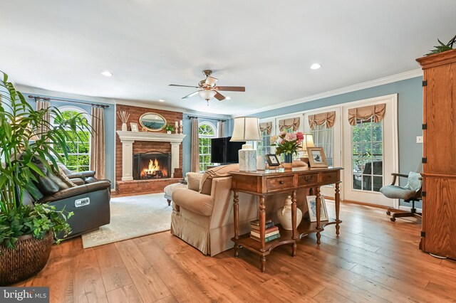 living area with crown molding, ceiling fan, a brick fireplace, light wood-style flooring, and recessed lighting