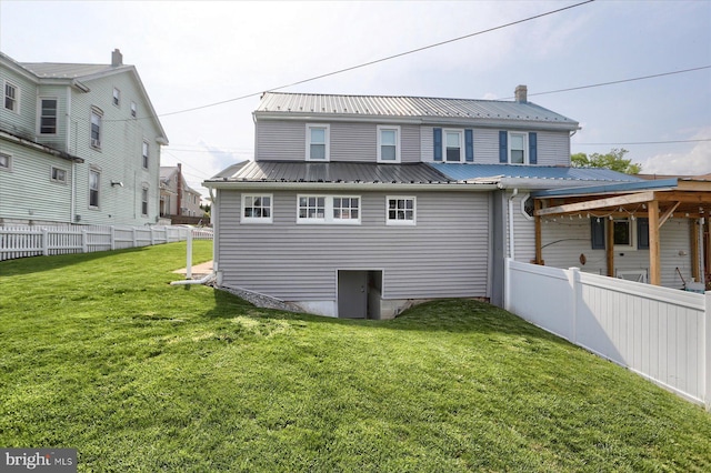 back of property featuring fence, a lawn, and metal roof