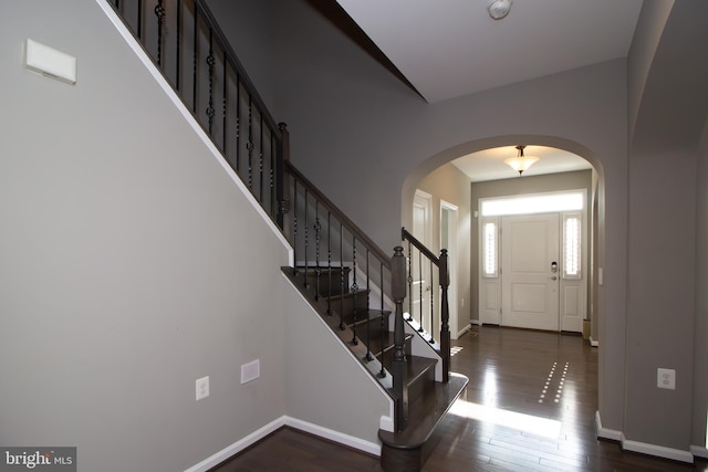 foyer entrance featuring baseboards, arched walkways, wood finished floors, and stairway