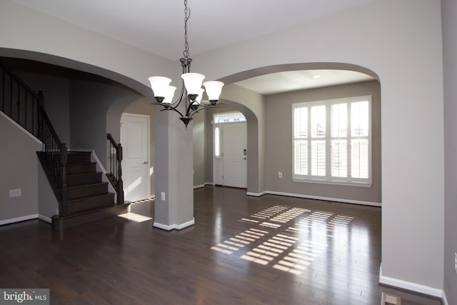 foyer entrance with baseboards, arched walkways, a notable chandelier, and stairway