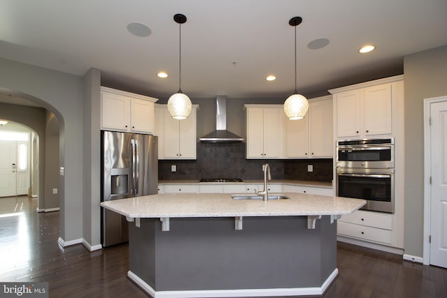 kitchen with wall chimney range hood, arched walkways, a sink, backsplash, and stainless steel appliances