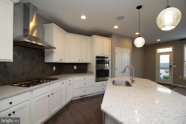 kitchen with wall chimney exhaust hood, white cabinetry, a sink, appliances with stainless steel finishes, and backsplash