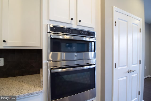 kitchen with double oven, backsplash, white cabinets, and light stone counters