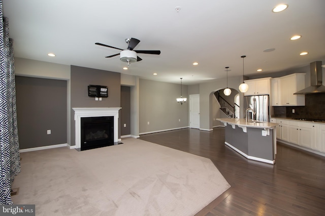 kitchen with wall chimney range hood, a breakfast bar, stainless steel fridge with ice dispenser, ceiling fan with notable chandelier, and recessed lighting