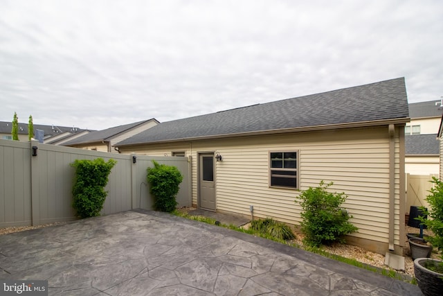 rear view of house featuring a patio, a fenced backyard, and roof with shingles
